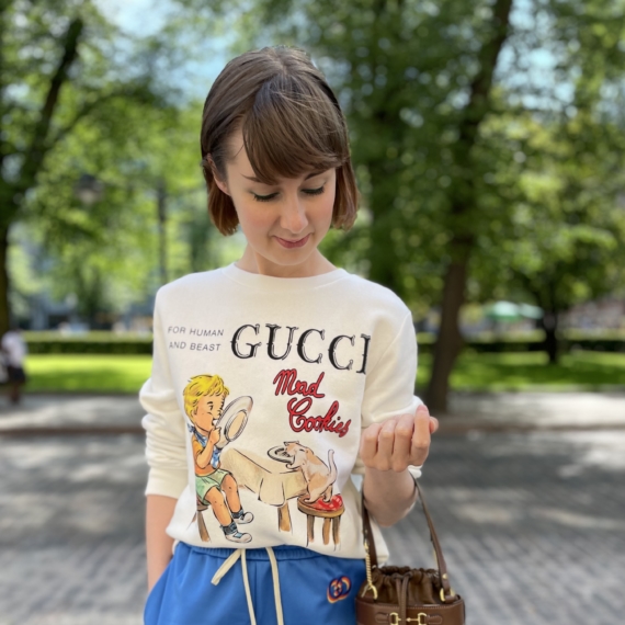 Naisella yllään Guccin college, shortsit ja käsivarrellaan laukku.
